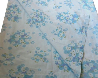 Puede incluir: Una sábana de cama azul claro con un estampado floral blanco y azul. La sábana está doblada y tiene una textura suave.