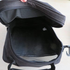 May include: Open black fabric bag with a zipper closure. The bag has a mesh pocket and a handle. The interior of the bag is visible, showing a spacious compartment. A hook is attached to the side of the bag.
