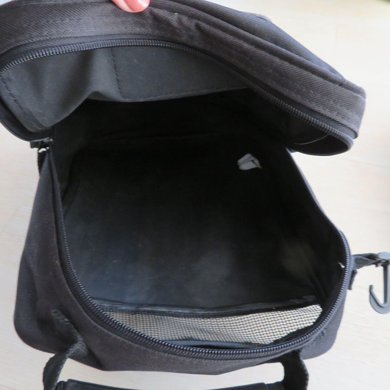 May include: Open black fabric bag with a zipper closure. The bag has a mesh pocket and a handle. The interior of the bag is visible, showing a spacious compartment. A hook is attached to the side of the bag.