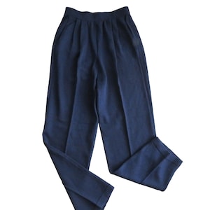 May include: Navy blue pleated pants with a relaxed fit. The pants have a high waist and pockets. The fabric appears to be a medium-weight material, suitable for various seasons. The pants are folded, showcasing the tailored design.