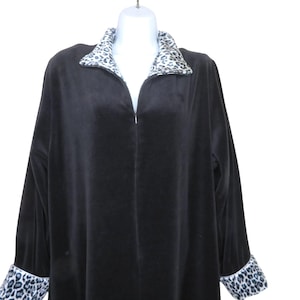 May include: A black velvet robe with a zip-up front, long sleeves, and a shawl collar. The collar and cuffs feature a contrasting leopard print pattern. The robe is displayed on a white mannequin.