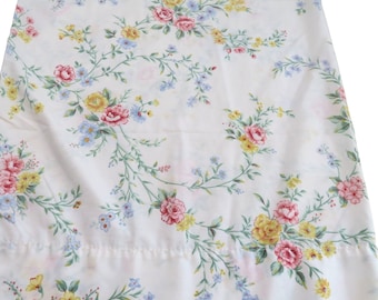 May include: White fabric with a floral pattern featuring pink, yellow, and blue flowers. The flowers are arranged in a repeating pattern on a white background.