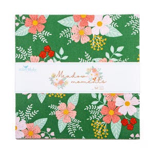 May include: A stack of fabric squares with a floral pattern. The fabric features pink, peach, and white flowers with green leaves on a dark green background. The text "Meadow moments" is printed on a white band.