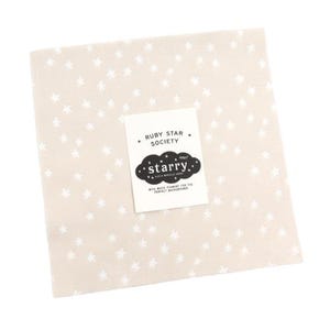 May include: A square, beige fabric with a repeating pattern of white stars. A white label with the text "RUBY STAR SOCIETY" and "starry." is centered on the fabric. The label also includes the text "WITH WHITE PIGMENT FOR THE PERFECT BACKGROUND."