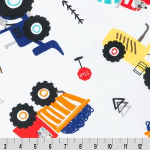 May include: White fabric with a colorful print featuring cartoon tractors, stop signs, and geometric shapes. The tractors are yellow, blue, and red, with black wheels. The stop signs are red with white text. The fabric has a ruler at the bottom.