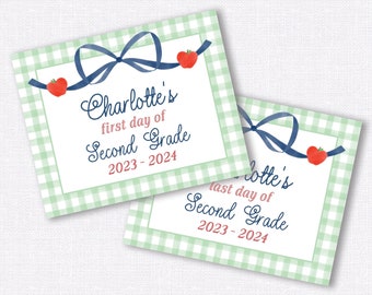 May include: Two green and white gingham patterned gift tags with blue bows and red apple accents. The top tag says "Charlotte's first day of Second Grade 2023 - 2024". The bottom tag says "Charlotte's last day of Second Grade 2023 - 2024".