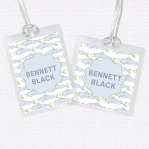 May include: Two white luggage tags with a blue and green fish pattern. The tags have a blue and white scalloped label with the text "BENNETT BLACK" on each.