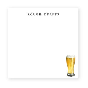May include: A white notepad with the text "ROUGH DRAFTS" printed at the top. A glass of beer with a white head is pictured in the bottom right corner.