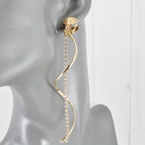 May include: Gold clip-on earring with a long, dangling chain of sparkling rhinestones. The chain is twisted into a spiral shape.