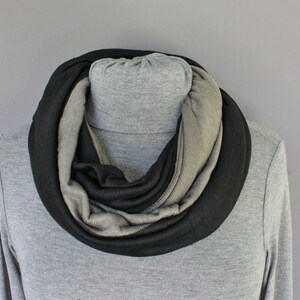 May include: A black and gray infinity scarf made of soft fabric. The scarf is folded in a circle and is displayed on a gray mannequin.