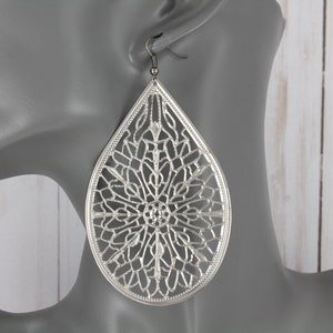May include: Silver teardrop-shaped earrings with a delicate, intricate, cut-out design.