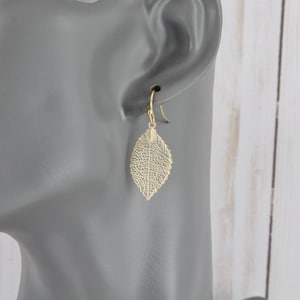 May include: Gold leaf earrings with a delicate, intricate design. The earrings are dangle style and feature a leaf shape.