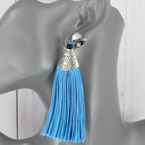 May include: A pair of blue tassel earrings with silver and black accents. The earrings are clip-on style.