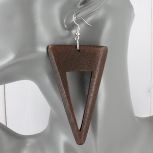 May include: A pair of large, brown wooden triangle earrings with a cut-out triangle in the center. The earrings have silver hooks.
