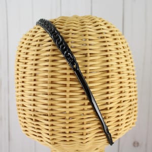 May include: Black plastic headband with a chain-like design. The headband is on a wicker display stand.