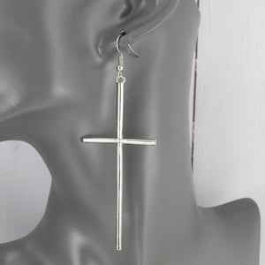 May include: Silver cross dangle earrings. The cross is long and thin, with a simple design.
