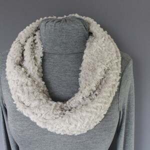May include: A soft, light beige faux fur infinity scarf. The scarf is made of a fluffy, fuzzy material and is perfect for keeping warm in the winter.