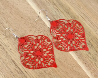 May include: A pair of red dangle earrings with a delicate, intricate floral design. The earrings are made of metal and have a silver hook closure.