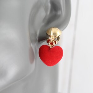 May include: Red heart-shaped clip-on earrings with a gold-tone metal clasp. The heart is made of a soft, fuzzy material.