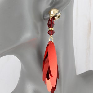 May include: Red dangle earrings with a gold clip-on closure. The earrings feature a cascade of red sequins and a red crystal bead.