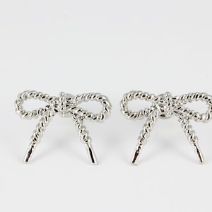 May include: A pair of silver bow-shaped earrings with a twisted rope design.