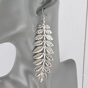 May include: Silver dangle earrings with a leaf design. The earrings are long and feature multiple leaves.