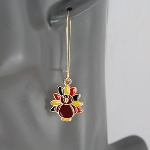 May include: Gold dangle earrings with a red, yellow, and black turkey charm.