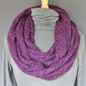 May include: A purple infinity scarf with a cable knit pattern and flecks of orange and yellow throughout.