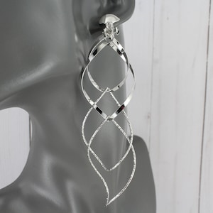 May include: Silver clip-on earrings with a twisted, layered design. The earrings are long and dangle, with a geometric shape.