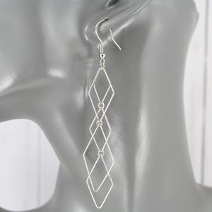 May include: Silver geometric dangle earrings with a diamond shape design. The earrings are long and feature multiple connected diamond shapes.