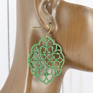 May include: Green wooden earrings with a delicate, intricate, laser-cut design. The earrings are shaped like a flower with a circular center and multiple layers of petals.
