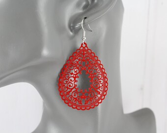 May include: Close-up of a red filigree teardrop earring with a silver hook. The earring features an intricate, openwork design with a scalloped edge. The earring is displayed on a mannequin.