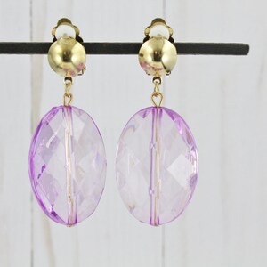 May include: A pair of purple clip-on earrings with gold-tone metal accents. The earrings feature large, round, faceted purple stones.
