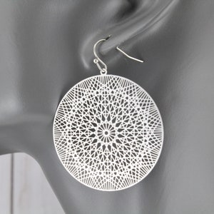 May include: Silver tone geometric circle earrings with a delicate, intricate design. The earrings are lightweight and dangle from a simple hook.