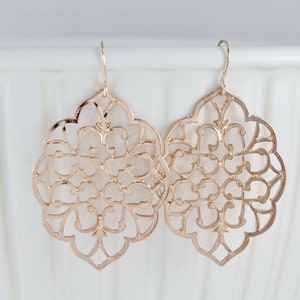 May include: A pair of gold-tone earrings with a delicate, intricate filigree design. The earrings are shaped like a flower with a circular center and multiple layers of petals.