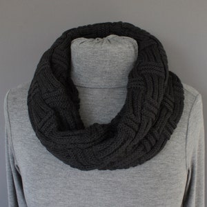 May include: A black knitted infinity scarf with a cable knit pattern.