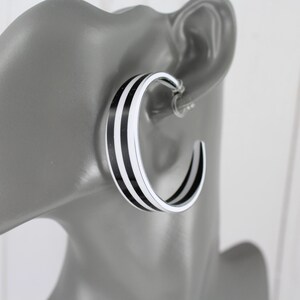 May include: Black and white striped hoop earrings. The earrings are large and have a thick band.