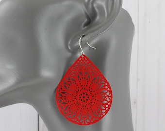 May include: Red dangle earrings with a laser cut design in the shape of a teardrop. The earrings are made of metal and have a silver hook.