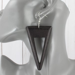 May include: A pair of large, black wooden triangle earrings with a cut-out triangle in the center. The earrings are hanging from silver hooks.