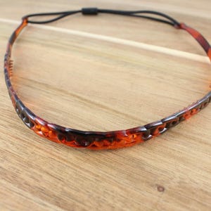 May include: A brown and black plastic headband with a textured design. The headband is made of a flexible material and has a stretchy elastic band.
