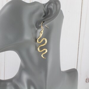 May include: Gold snake dangle earrings. The snake is curled in a realistic pose and hangs from a simple hook.