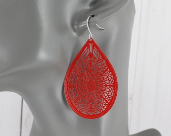 May include: Red teardrop-shaped earrings with a delicate, intricate laser-cut design. The earrings are made of metal and have a shiny finish.