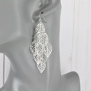 May include: Silver dangle earrings with a layered leaf design. The earrings are delicate and feminine.