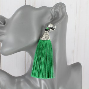 May include: Green tassel earrings with a silver, ornate, triangular pendant.