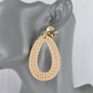 May include: A pair of beige woven oval-shaped earrings with gold-tone clip-on closures.