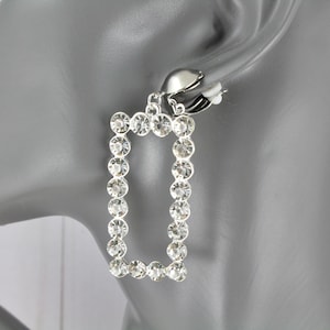May include: Silver clip-on earrings with a rectangular frame made of clear rhinestones.