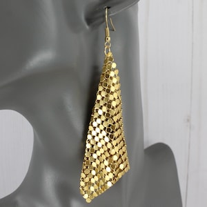 May include: Gold-toned, dangling earrings with a triangular shape. The earrings are made of small, circular metal pieces linked together, creating a mesh-like appearance. The hook is a simple, curved design.