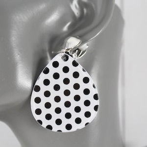 May include: A teardrop-shaped earring featuring a white base with a repeating black polka dot pattern. The earring is attached to a silver-toned metal clip-on mechanism, designed for secure placement on the earlobe without the need for a piercing.
