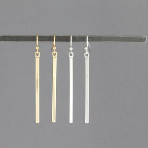 May include: Four pairs of long, thin dangle earrings. Two pairs are gold, one pair is silver, and one pair is a lighter shade of silver.