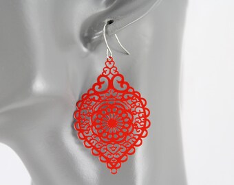 May include: A single red filigree earring with a silver hook. The earring has a diamond shape with an intricate openwork design. The red color is vibrant and eye-catching, and the earring is shown against a gray background.